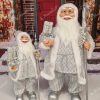 Dekoration Weihnachtsmann Eisig, Er trägt einen silbernen Mantel mit Pelzbesatz und hält Geschenke in der Hand.