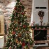 Künstlicher grüner Weihnachtsbaum, geschmückt mit roten und goldenen Ornamenten im Wohnzimmer am Kamin