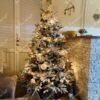 Schneebedeckter künstlicher Weihnachtsbaum mit weißen Ornamenten im Wohnzimmer