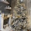 Mit Schnee bedeckter künstlicher Weihnachtsbaum mit weißen und goldenen Dekorationen im Wohnzimmer