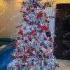 Künstlicher, schneebedeckter Weihnachtsbaum mit weißen und roten Dekorationen im Wohnzimmer