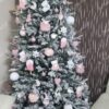 Ein schneebedeckter künstlicher Weihnachtsbaum mit weißen und rosa Dekorationen im Wohnzimmer