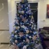 Großer und breiter künstlicher Weihnachtsbaum mit weißen und goldenen Verzierungen im Wohnzimmer