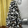 Ein grüner künstlicher Weihnachtsbaum, geschmückt mit weißem Weihnachtsschmuck, im Wohnzimmer