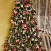 Ein hoher künstlicher Weihnachtsbaum, geschmückt mit Weihnachtsschmuck aus Holz und Stroh, im Wohnzimmer