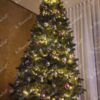 Ein hoher künstlicher Weihnachtsbaum, geschmückt mit silbernen und violetten Weihnachtsdekorationen, im Wohnzimmer