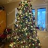 Ein hoher künstlicher Weihnachtsbaum, geschmückt mit rotem, blauem und grünem Weihnachtsschmuck, im Wohnzimmer