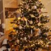 Hellgrüner künstlicher Weihnachtsbaum, geschmückt mit weißen und goldenen Weihnachtsdekorationen mit warmweißer Beleuchtung, im Wohnzimmer