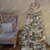 Ein niedriger schneebedeckter künstlicher Weihnachtsbaum, geschmückt mit rosa und silbernen Weihnachtsdekorationen, mit weißer Beleuchtung, im Wohnzimmer,