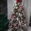 Ein schneebedeckter künstlicher Weihnachtsbaum, dicht mit rot-weißem Weihnachtsschmuck geschmückt, im Wohnzimmer,
