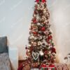 Ein schmaler künstlicher Weihnachtsbaum, geschmückt mit rotem und goldenem Weihnachtsschmuck, im Wohnzimme