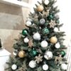 Ein kleiner künstlicher Weihnachtsbaum mit silbergrünen Zweigen, geschmückt mit silbergoldenem und grünem Weihnachtsschmuck, im Wohnzimmer,