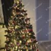 Ein klassischer künstlicher Weihnachtsbaum mit versilberten Zweigenden und Eiskristallen, geschmückt mit rotem und goldenem Weihnachtsschmuck, im Wohnzimmer