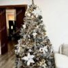 Künstlicher Weihnachtsbaum mit schneebedeckten Zweigen, geschmückt mit weißen und goldenen Weihnachtsdekorationen, im Wohnzimmer