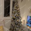 Ein schmaler künstlicher Weihnachtsbaum mit schneebedeckten Ästen, geschmückt mit goldenem Weihnachtsschmuck, im Wohnzimmer