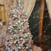 Künstlicher Weihnachtsbaum mit schneebedeckten Zweigen, geschmückt mit rosa und weißen Weihnachtsdekorationen, im Wohnzimmer
