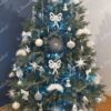 Künstlicher Weihnachtsbaum mit silbergrünen Ästen, geschmückt mit weiß-silbernem Weihnachtsschmuck, im Wohnzimmer