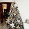 Künstlicher Weihnachtsbaum mit schneebedeckten Zweigen, verziert mit weißen und goldenen Weihnachtsornamenten, mit warmweißer Beleuchtung im Wohnzimmer