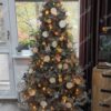 Künstlicher Weihnachtsbaum mit silbergrünen Zweigen, dekoriert mit weißem und natürlichem Weihnachtsschmuck, mit warmweißer Beleuchtung im Wohnzimmer