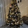 Dichter grüner künstlicher Weihnachtsbaum mit weißen und goldenen Verzierungen, mit warmweißer Beleuchtung, im Wohnzimmer