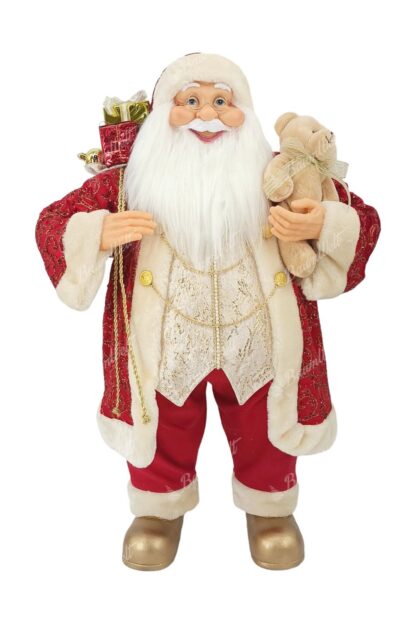 Dekoration Santa Claus Rot-Gold 80cm er trägt einen roten Mantel mit goldenen Verzierungen und einer Kette. er hat goldene Schuhe an. Sie hat einen langen weißen Bart, eine Brille undhält ein Kuscheltier in der Hand.